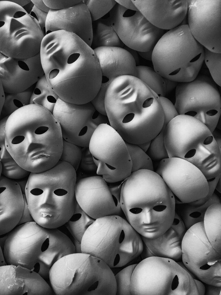 A pile of expressionless, hollow masks in grayscale, symbolizing the facades people wear and the hidden pain behind them.