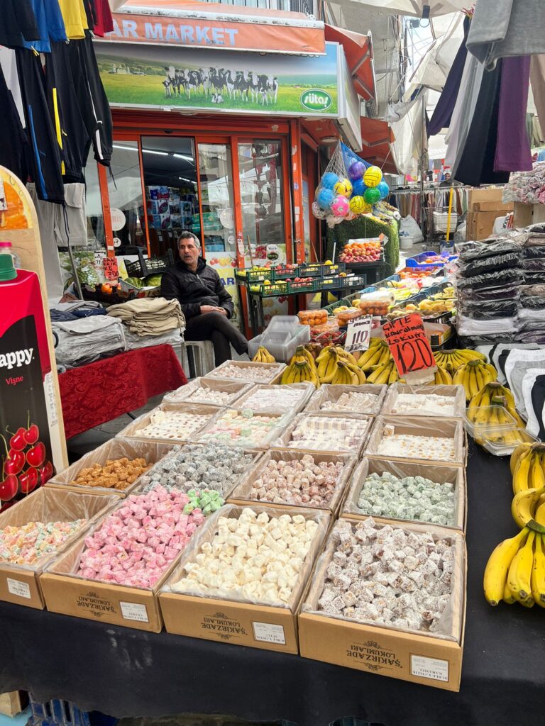 Assorted Turkish delights and fresh fruits on display at a vibrant market stall in Fatih Çarşamba Pazarı, Istanbul.